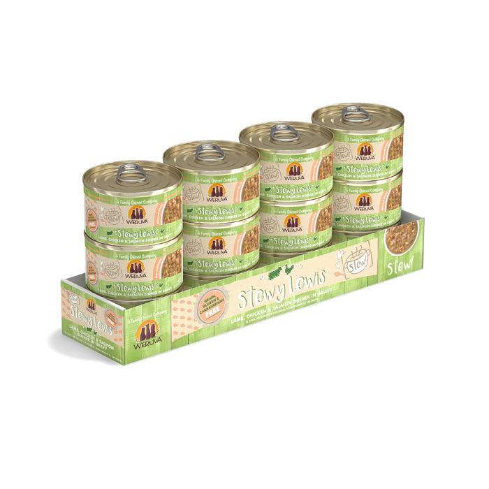 Six cans of Weruva Stewy Lewis cat food, featuring chicken, grass-fed lamb, and mackerel stew, are arranged in a green cardboard tray. The cans display beige labels with images of the stew and the Weruva brand logo.